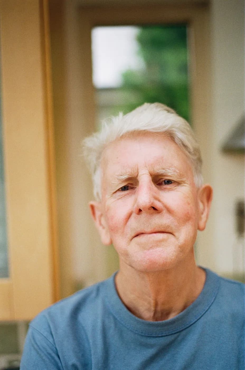 Portrait of a man with short white hair wearing a blue shirt