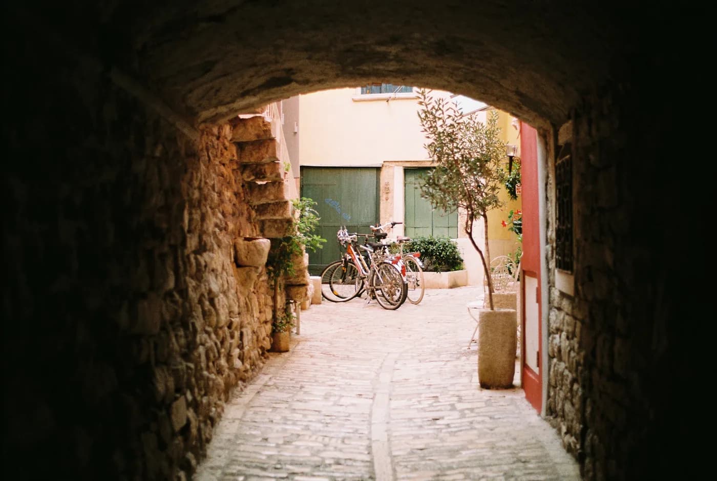 Sunlit courtyard and bicycles framed by a dark stone arch